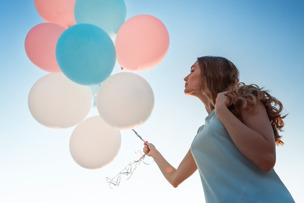 空を背景に色とりどりの風船を飛んでいる若い美しい女性。幸せと夢のコンセプト