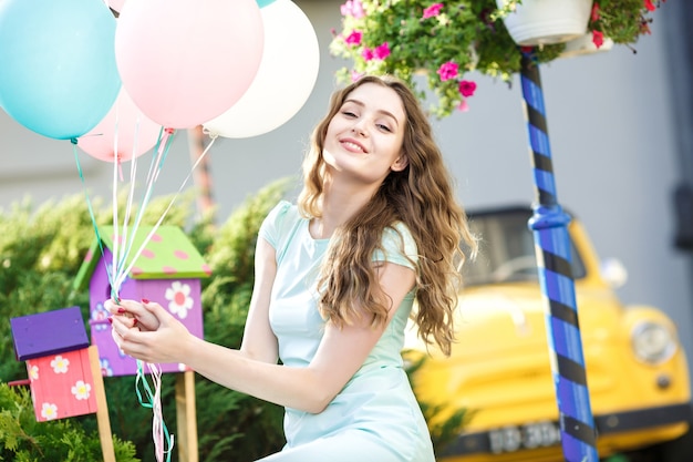 Young beautiful woman with flying multicolored balloons in the city