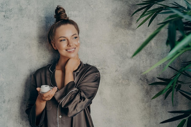 Young beautiful woman with glowing healthy skin broadly smiling while holding face cream