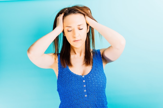 Young beautiful woman with hands on head with pain stressed head with blue background