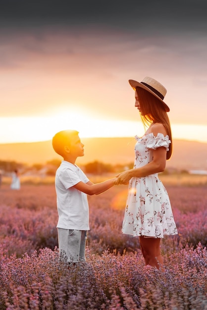 그녀의 아들과 함께 젊은 미녀가 아름다운 라벤더 밭을 걷고 꽃 향기를 즐기고 있습니다 휴식과 아름다운 자연 라벤더 꽃과 꽃 따기