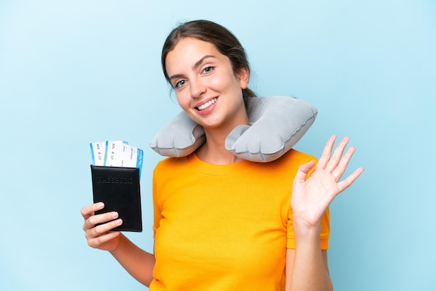 Foto giovane bella donna con cuscino da viaggio gonfiabile isolato su sfondo blu che saluta con la mano con felice espressione