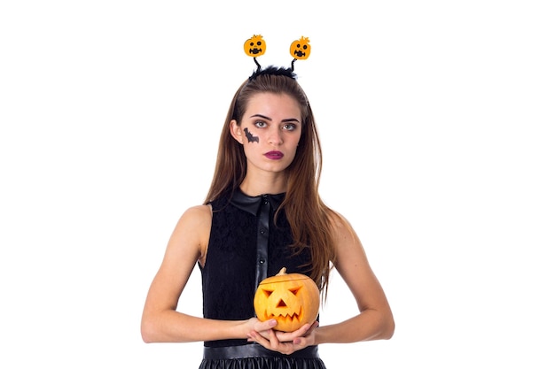 Young beautiful woman with little picture of bat on her cheeck and headband holding a pumpkin