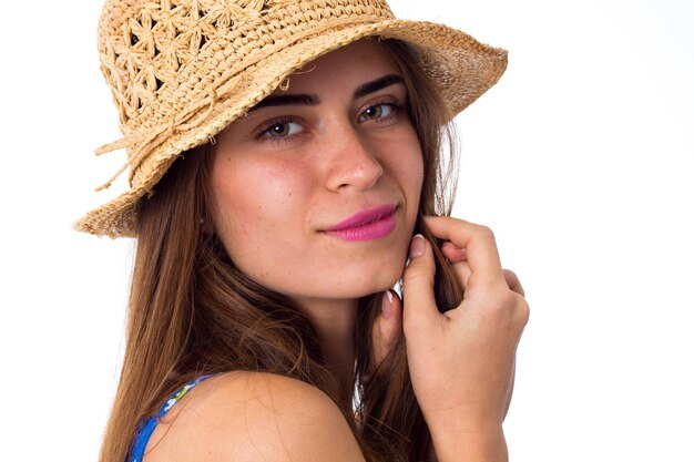 スタジオで白い背景に微笑んでかわいい帽子と青いシャツの長い茶色の髪の若い美しい女性