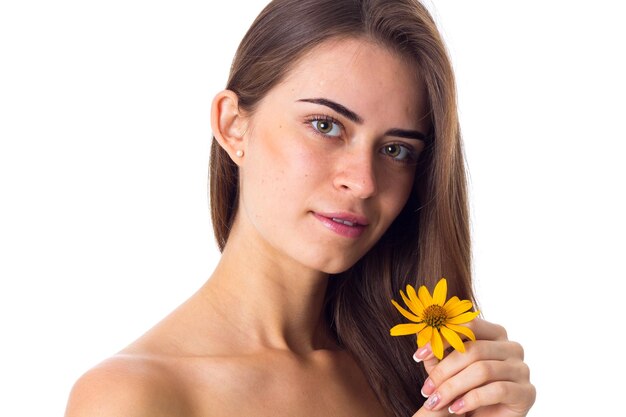 Young beautiful woman with long brown hair holding yellow flower on white background in studio