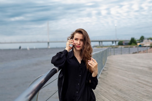 Young beautiful woman with long brunette hair looking at the sea and speaking on mobile phone