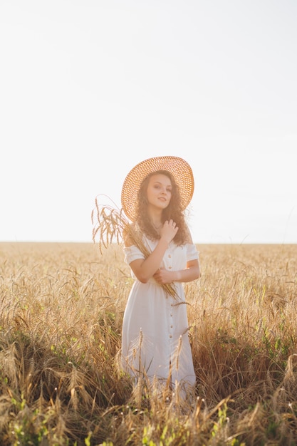 Young beautiful woman with long curly hair poses in a wheat field in the summer at sunset