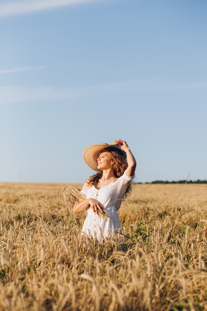 Young beautiful woman with long curly hair poses in a wheat field in the summer at sunset