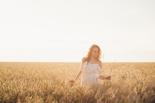 Young beautiful woman with long curly hair poses in a wheat field in the summer at sunset