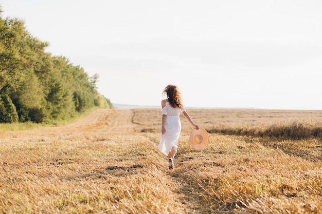 Young beautiful woman with long curly hair poses in a wheat field in the summer at sunset