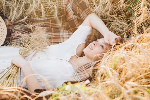 Giovane bella donna con lunghi capelli ricci pone in un campo di grano in estate al tramonto