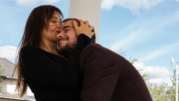 A young beautiful woman with long dark hair kisses on the forehead her boyfriend in the street