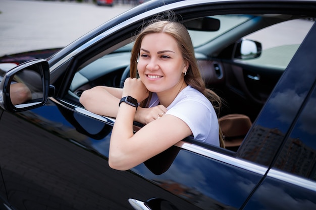 駐車場の黒い車に長い髪の若い美しい女性が座っています。カジュアルな服装の可愛い女の子。車の旅