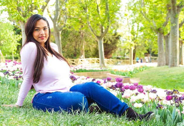 Young beautiful woman with long hair sitting in a park meadow with tulips