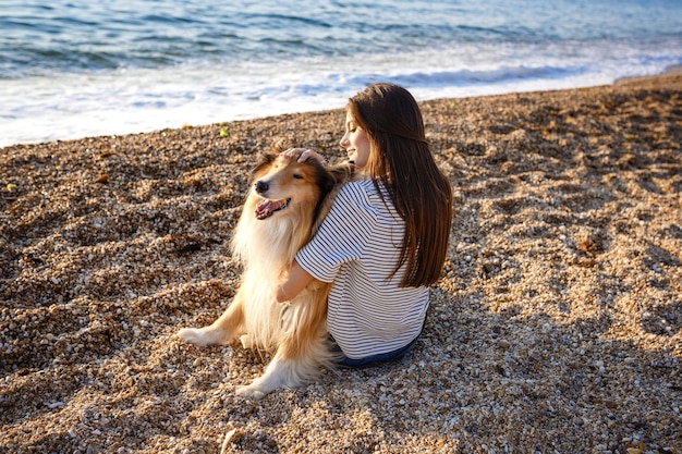 コリー犬と一緒に歩く長い髪の若い美しい女性。公園の屋外。海の近く、夏のビーチ