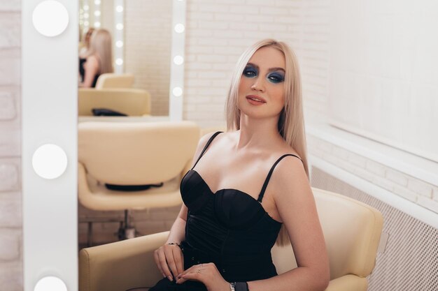 Young beautiful woman with long healthy blonde hair looking at the mirror in hairdressing salon