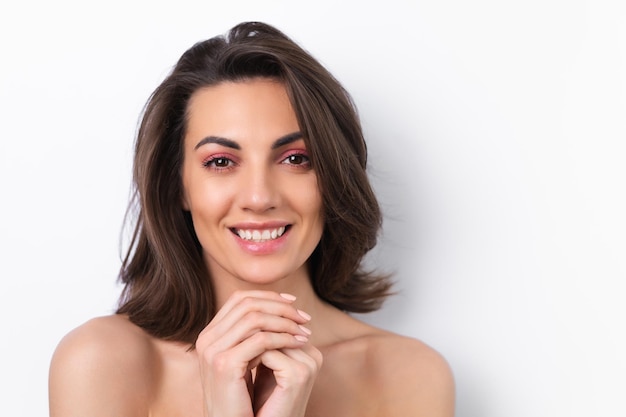 Young beautiful woman with perfect skin bright spring pink makeup and naked shoulders on a white background Cheerfully smiles