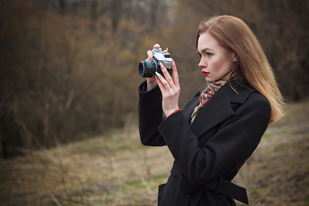 young beautiful woman with a photo camera in her hands takes pictures of nature in autumn.