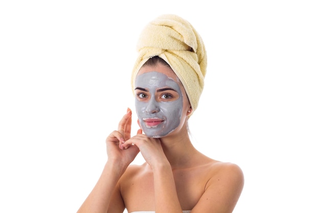 Young beautiful woman with yellow towel on her head and blue cosmetic mask touching her face