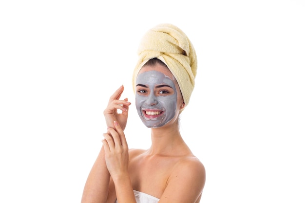 Young beautiful woman with yellow towel on her head and blue cosmetic mask touching her face