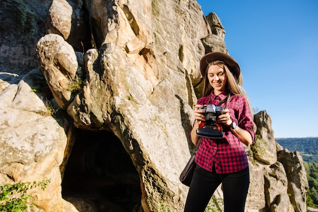 Young beautiful woman witn vintage photocamera on the rocky mountains with scenic landscape on the background