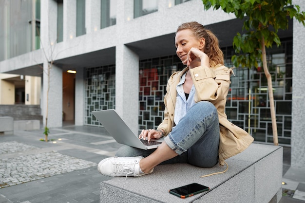 Young beautiful woman working on a laptop sitting on the bench in the street