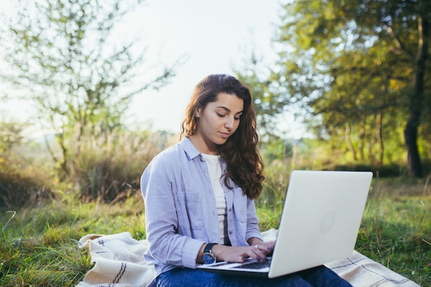 Young beautiful  woman working on a laptop sitting on the grass