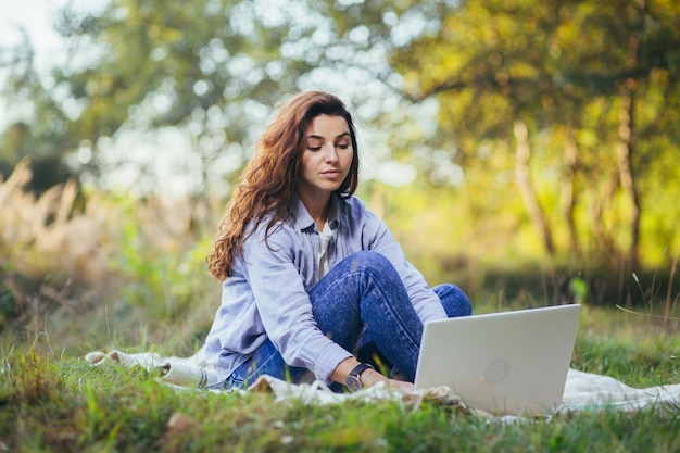 Young beautiful  woman working on a laptop sitting on the grass