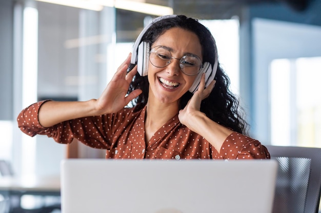 young beautiful woman working in the office at the workplace closeup hispanic woman in headphones singing along and dancing joyfully business woman on break resting programmer happy