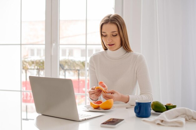 Young beautiful woman working with laptop at home in front of a large window with morning light