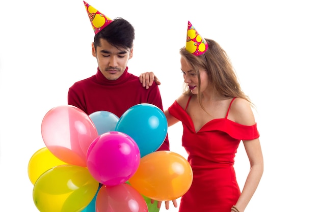 Young beautiful woman and young handsome man with celebrating hats holding many colored balloons