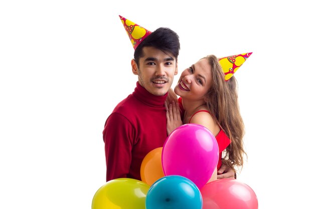 Giovane bella donna e giovane uomo bello con i cappelli celebrativi che tengono molti palloncini colorati