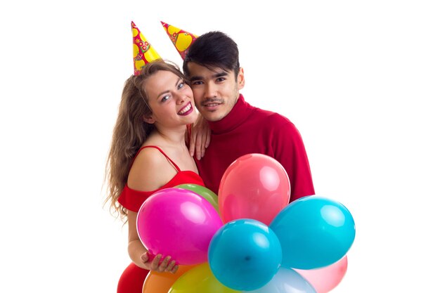 Young beautiful woman and young handsome man with celebrating hats holding many colored balloons