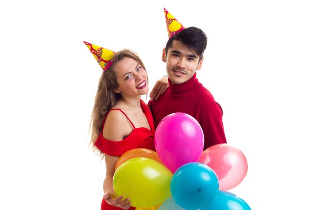 Young beautiful woman and young handsome man with celebrating hats holding many colored balloons