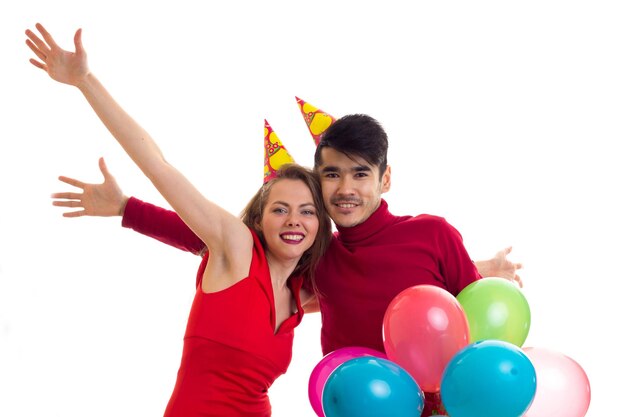 Young beautiful woman and young handsome man with celebrating hats holding many colored balloons