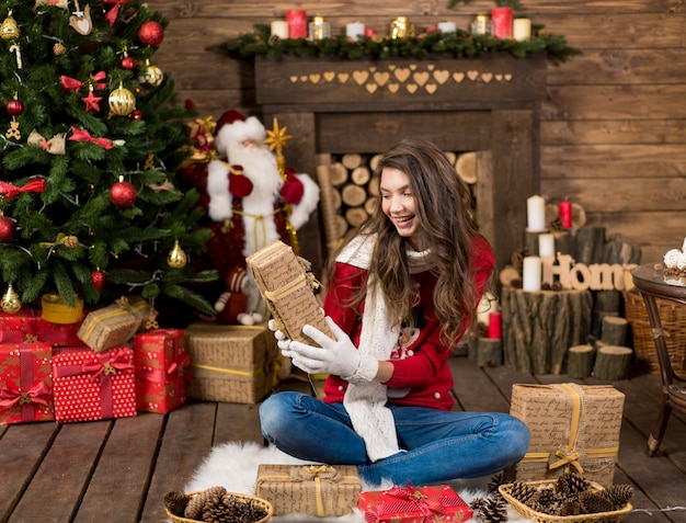 겨울에 젊은 아름다움 패션 신부 선물 상자를 들고 크리스마스 트리 근처에 앉아 겨울 옷을 입고 즐거운 여성 소녀.