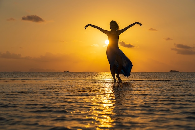 日没、タイ、パラダイス島の海の上の熱帯のビーチで踊っている若い美女がクローズアップ。夏のコンセプト。休日の旅行。