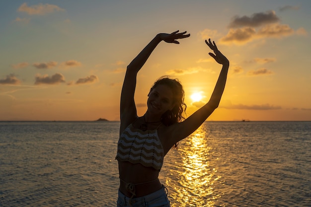 日没時の楽園の島の海の近くの熱帯のビーチで踊る若い美女