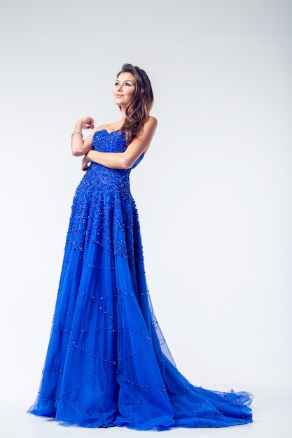 Young beauty woman in fluttering blue dress on a white wall