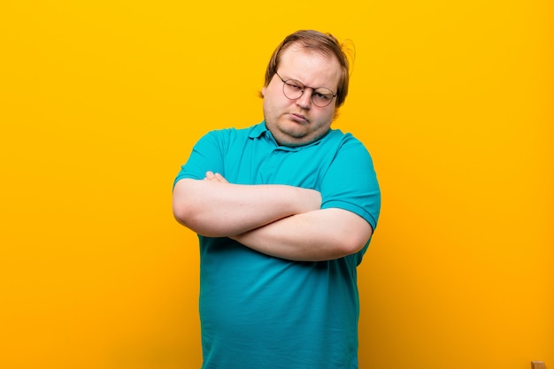 Young big size man feeling displeased and disappointed, looking serious, annoyed and angry with crossed arms on orange wall