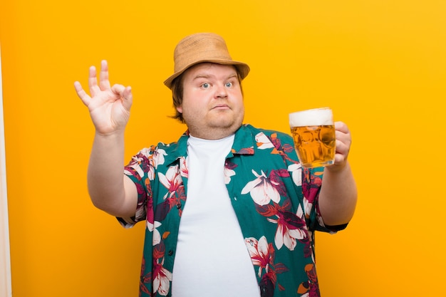 Young big size man with a pint of beer against flat wall