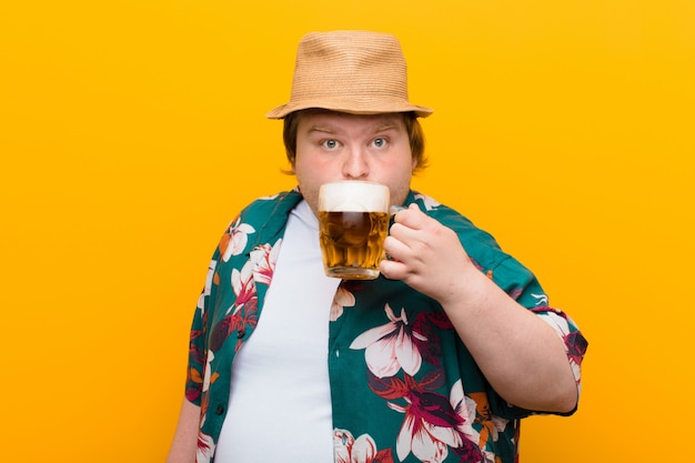 Young big size man with a pint of beer against flat wall