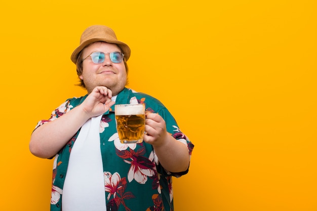 Young big size man with a pint of beer against flat wall