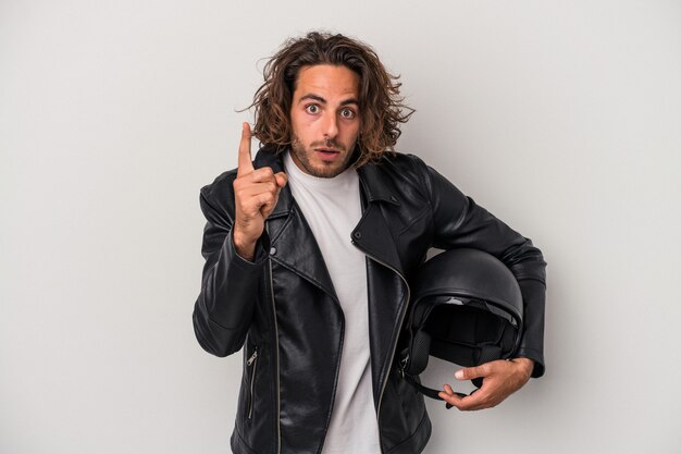 Young biker caucasian man holding a motorbike helmet isolated on gray background having an idea, inspiration concept.