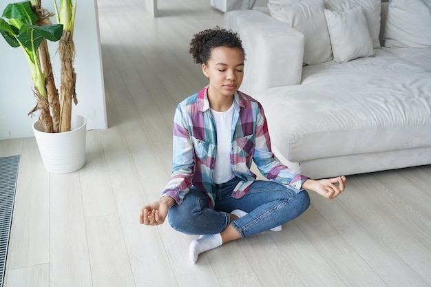 Young biracial girl practice yoga meditate do breathing exercises at home Stress relief wellness