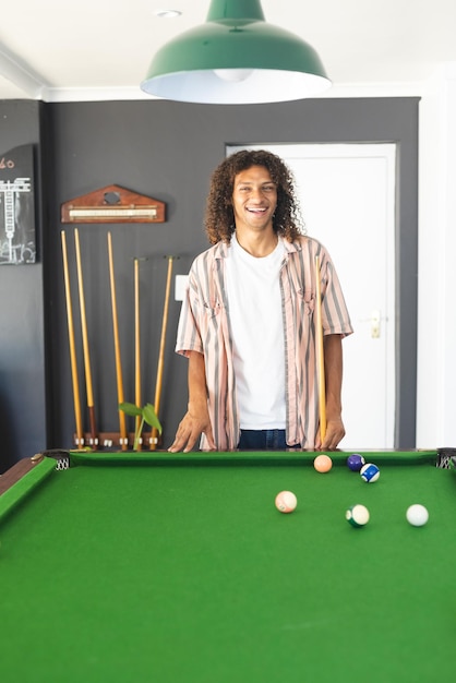 Young biracial man with curly hair stands by a pool table smiling