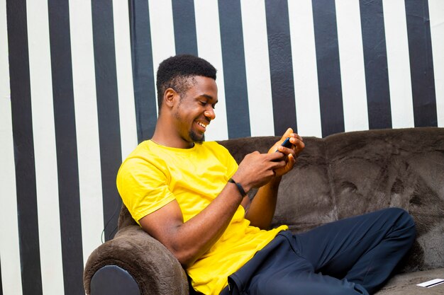 Young black african male hipster chatting with friends on
social network, read online news using mobile device during lock
down sitting at home