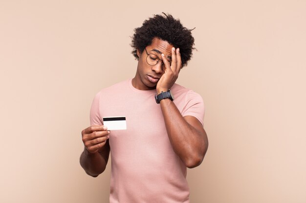 Young black afro man feeling bored, frustrated and sleepy after a tiresome, dull and tedious task, holding face with hand