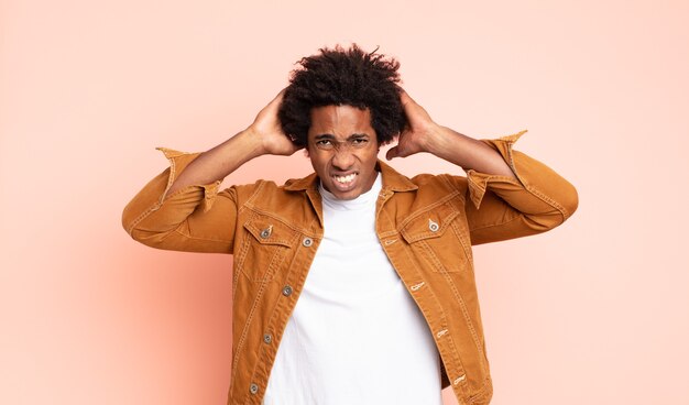 Foto giovane uomo afro nero che si sente stressato, preoccupato, ansioso o spaventato, con le mani sulla testa, in preda al panico per errore