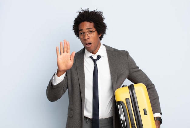 Young black afro man looking serious, stern, displeased and angry showing open palm making stop gesture